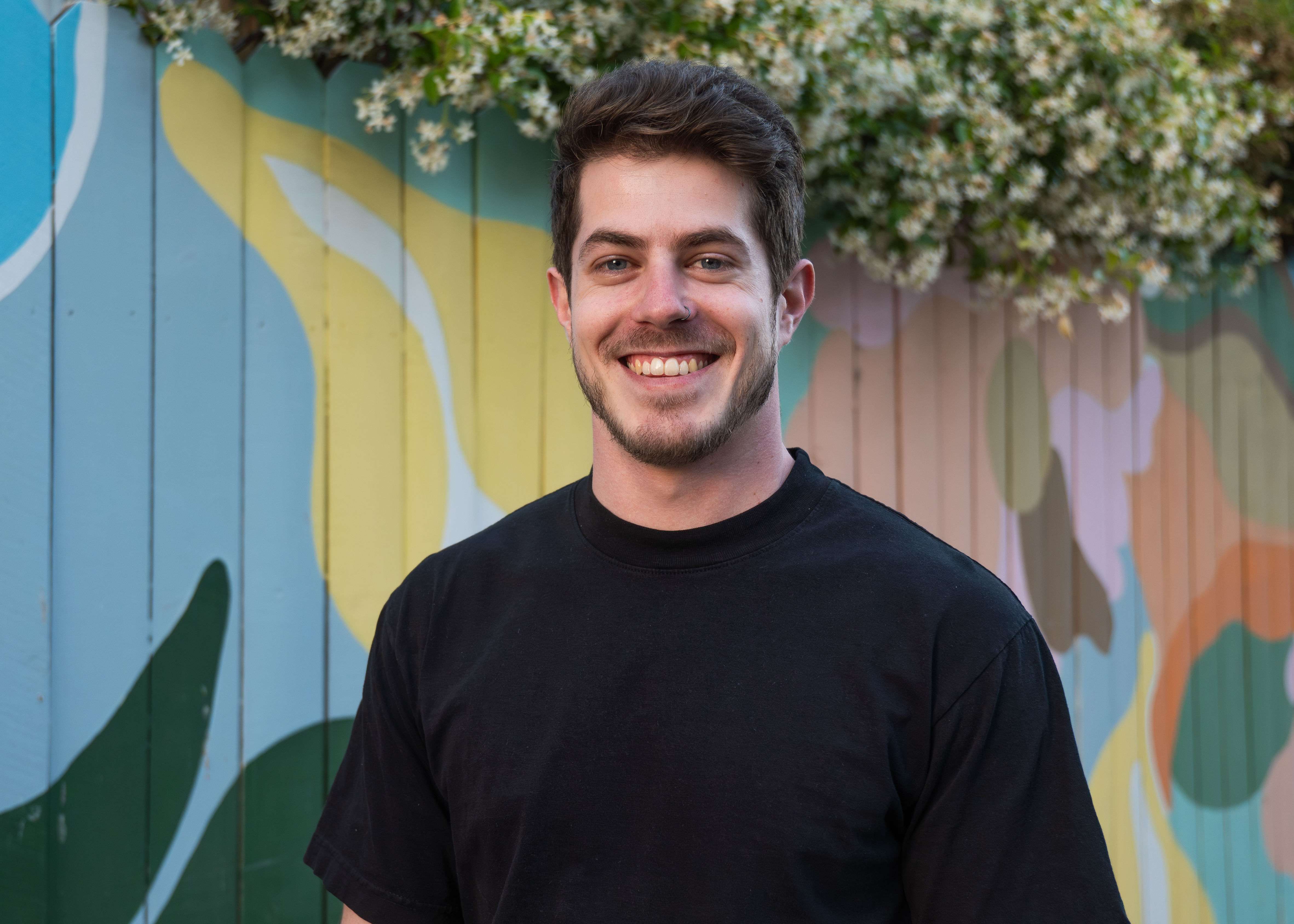 Headshot of Sasha with colorful fence in background